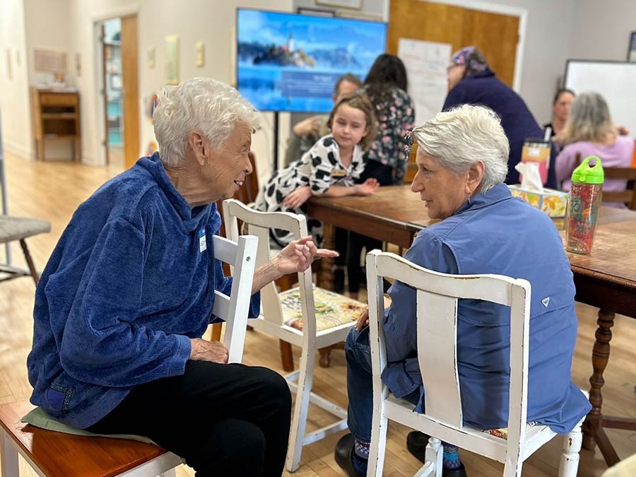 Photo of two women talking in a room full of people