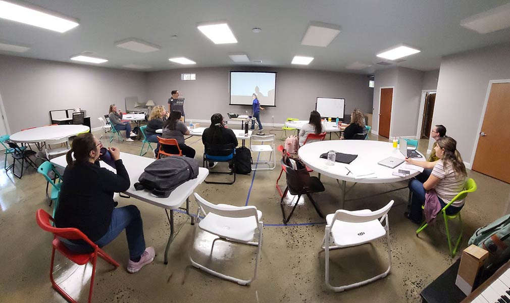 Photo of Teepa Snow in front of a projector screen presenting to a group of people