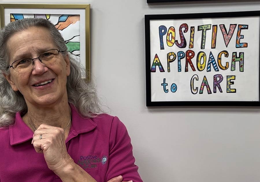 Photo of Teepa Snow next to Positive Approach to Care sign on wall